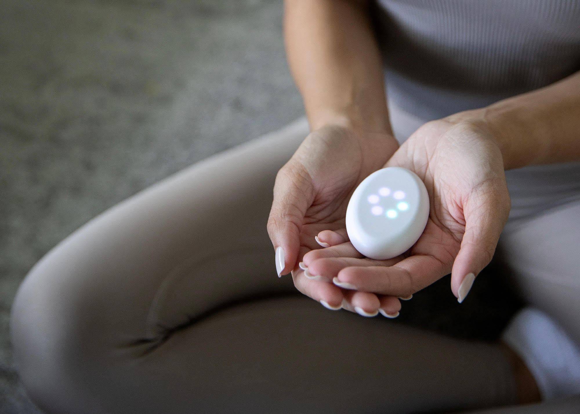 a person is seated, holding a biofeedback device in their hands that is showing a circle of colorful lights 